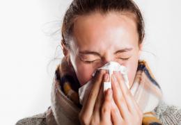 woman with fall scarf on sneezing into a tissue