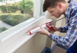 man applying sealant to a window