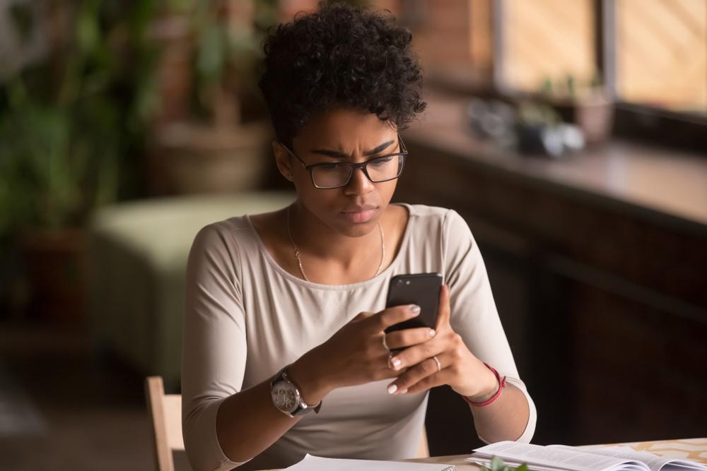 woman at home looking at phone confused