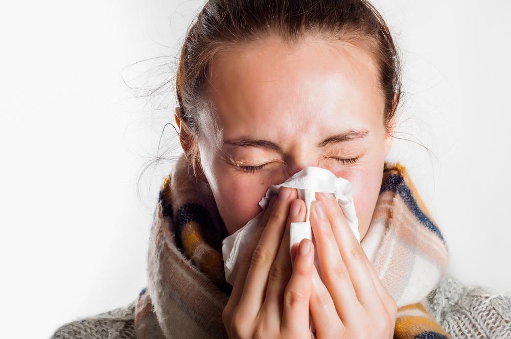 woman with fall scarf on sneezing into a tissue