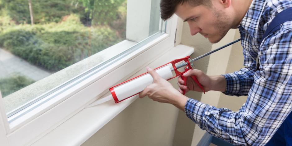 man applying sealant to a window